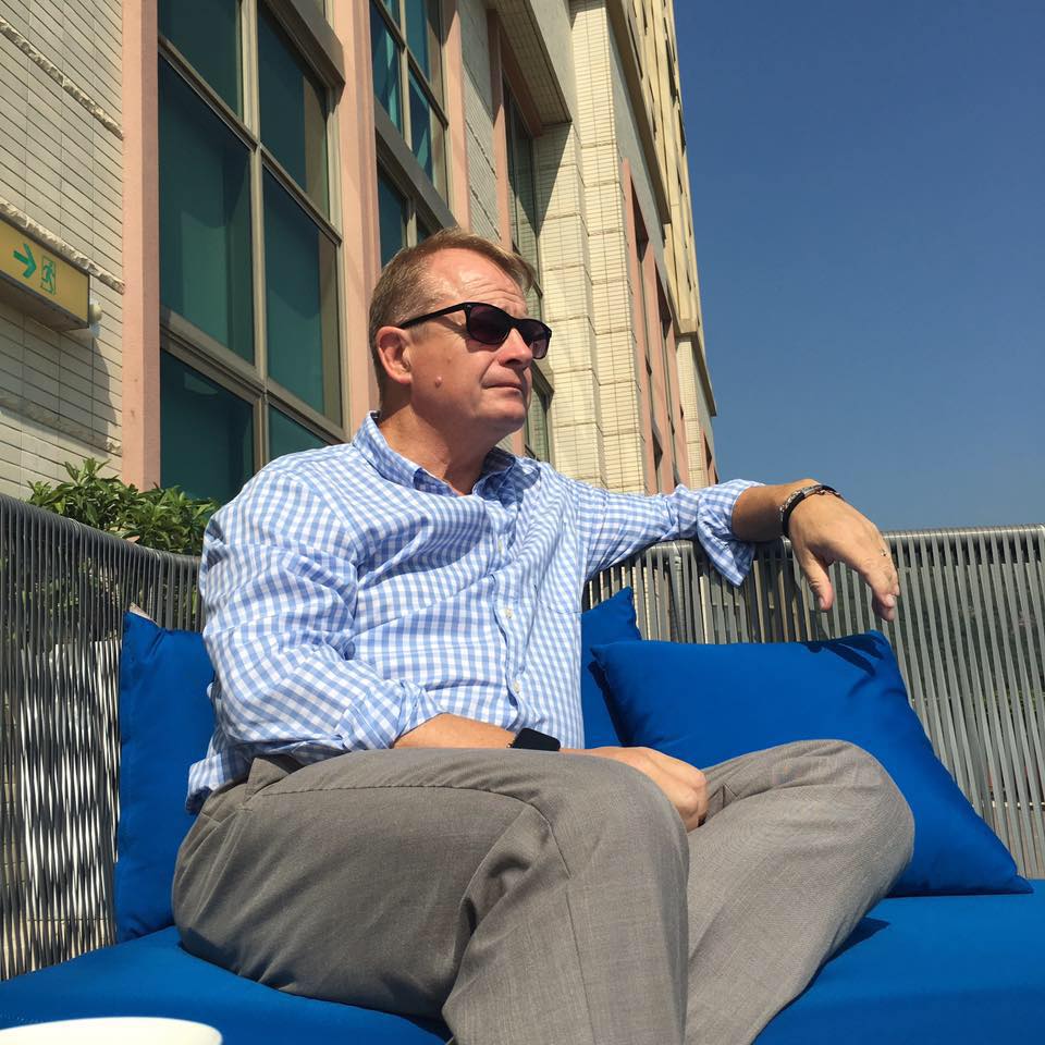 Man relaxing outdoors on a sunny day, sitting comfortably on a blue couch and enjoying the peaceful moment.